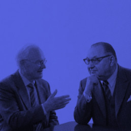 Jörg Koppenhöfer und Wilhelm Sander im Anzug im Gespräch an einem Tisch, künstlerisch in Blau dargestellt.